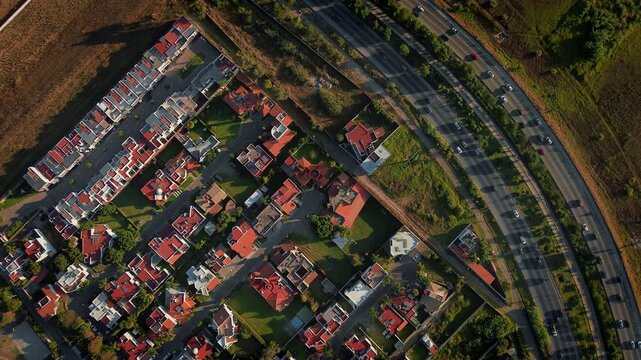 Aerial zenith drone reveals the Periferico Ecologico boulevard in Puebla with heavy traffic flowing alongside an upscale residential neighborhood during golden sunset light