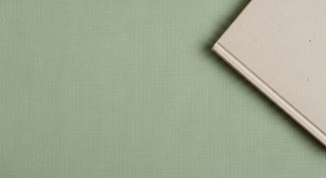 Minimalist book corner resting on sage green linen fabric texture background with soft natural lighting for organic flat lay mockup and aesthetic lifestyle composition.