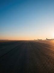 Fototapeta premium Two airplanes take off from a long airport runway. The sun rises in the distance, casting a warm glow on the tarmac.