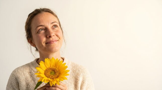 Woman holding a sunflower looking up with a gentle smile
