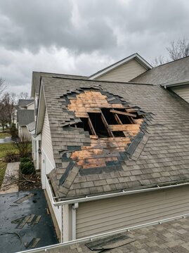 A damaged roof shows a large circular hole with exposed wood framing. The roof shingles are missing, revealing the interior of the house.