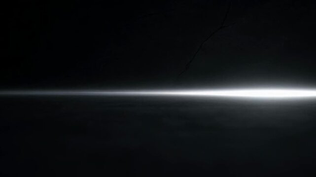 A thin horizontal beam of bright white light cutting through deep darkness.