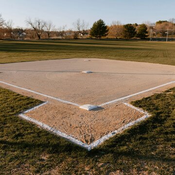 Empty baseball diamond with raked clay and chalked lines in a quiet park, featuring mown grass and trees for sports and recreation content