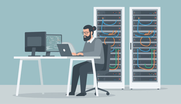 Bearded computer technician working on a laptop at his desk next to server racks with cables in a modern database center.