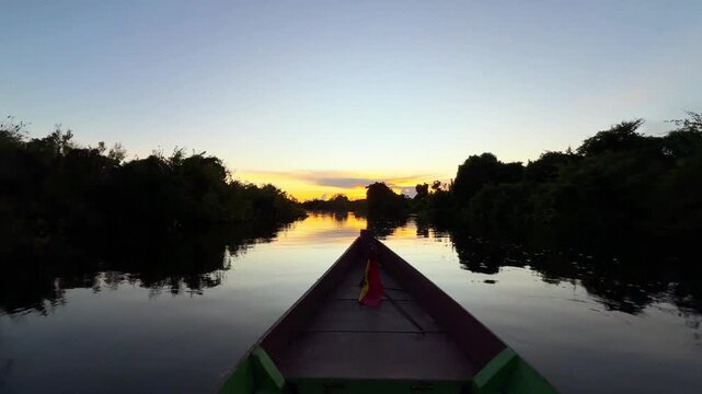 Wooden boat navigating a river in the Bolivian Amazon rainforest at sunset