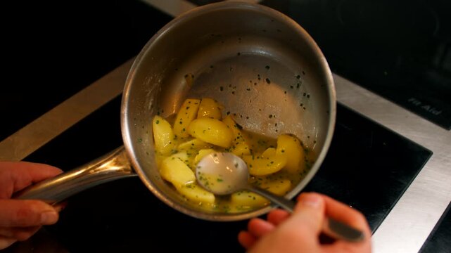 chef hand stirring ingredients in a hot saucepan with a tool on a restaurant kitchen stove. Professional culinary action and food preparation step details.