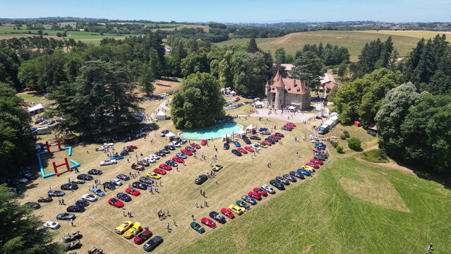 Succieu, France - 13 June 2026: Aerial view of the Chateau de Milliassieres during a car show with rows of colorful sports cars and people on the lawn surrounded by trees and rolling hills.