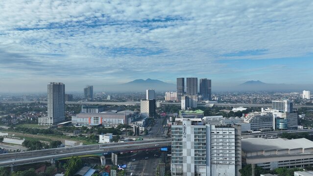Bekasi Barat, Indonesia - 12 April 2026: Aerial view of the city skyline featuring high-rise buildings, highway overpasses, and distant mountains under a cloudy sky.