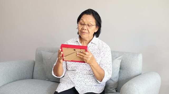 Asian Senior woman looks family photographs in living room, enjoy retirement life, missing husband and relative in house.