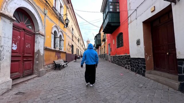 Man in Blue Hoodie Walking Down a Historic Cobblestone Street with Colorful Colonial Architecture in Potosi, Bolivia