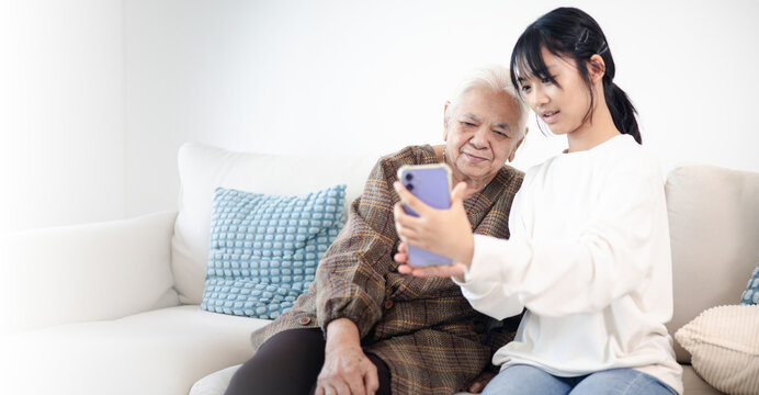 Happy teenage girl showing smartphone to senior woman at home, highlighting family bonding, digital communication, technology learning, and active aging.