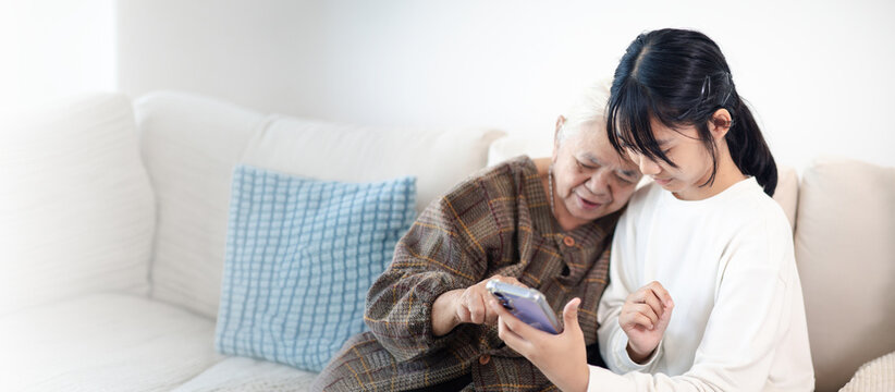 Happy teenage girl showing smartphone to senior woman at home, highlighting family bonding, digital communication, technology learning, and active aging.