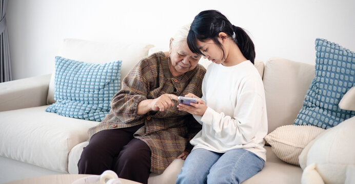 Happy teenage girl showing smartphone to senior woman at home, highlighting family bonding, digital communication, technology learning, and active aging.