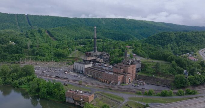 Aerial establishing of retired coal power station beside river and mountains, drone ascend angled view