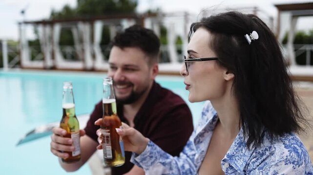 Happy couple relaxing together at the poolside while sipping refreshing drinks. Concept leisure, summer and happiness.
