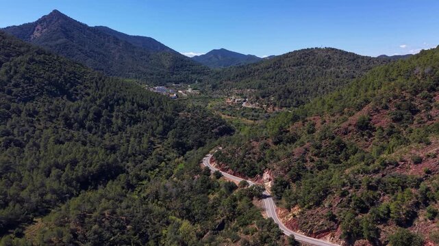 Sierra de Espada national park Spain, winding mountain road through dense pine forest valley with small village nestled among green hills under clear blue sky
