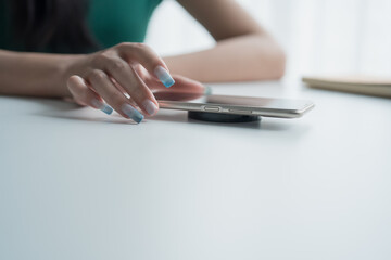 Fototapeta premium Charging mobile phone battery with wireless charging device in the table. Smartphone charging on a charging pad. Mobile phone near wireless charger Modern lifestyle technology.