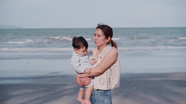 Young mother holding her adorable baby boy travel on the beach at sunny day.