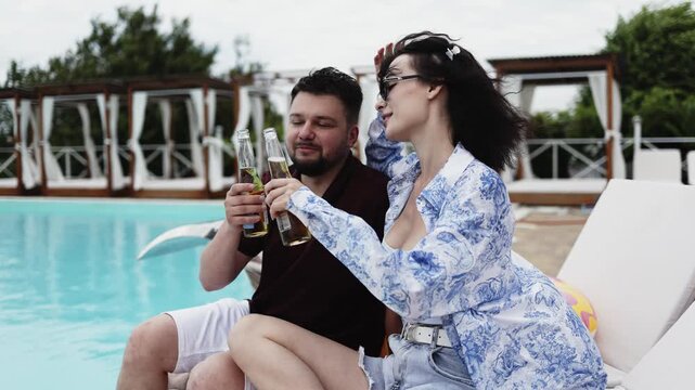 Young man and woman relaxing poolside with drinks during a sunny vacation day. Concept friendship, comfort and lifestyle.

