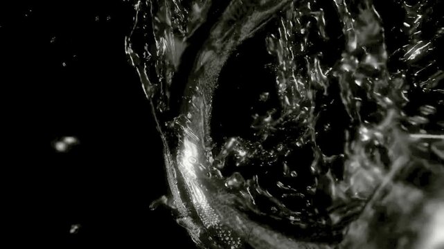 Slow motion macro shot of clear liquid splashing dynamically inside a glass against a black background