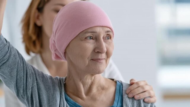 Mature woman wearing headscarf during physical therapy session with female therapist providing support and encouragement in bright room