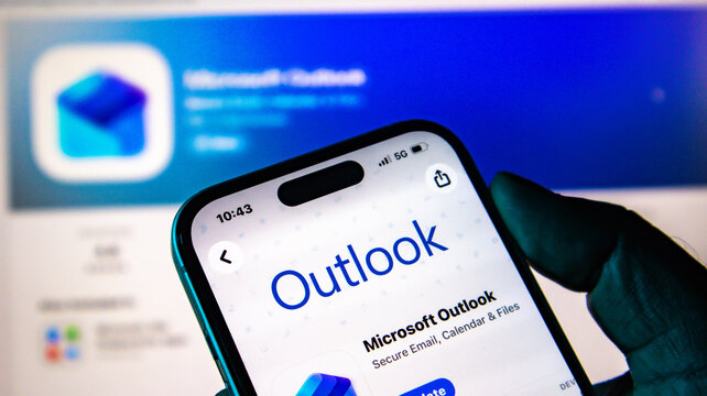 Closeup of a hand holding a smartphone displaying the microsoft outlook app store page on a blurred background
