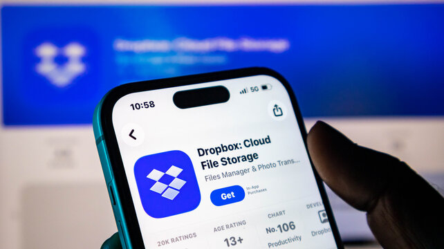 Closeup of a hand holding a smartphone displaying the dropbox app store page on a blurred background