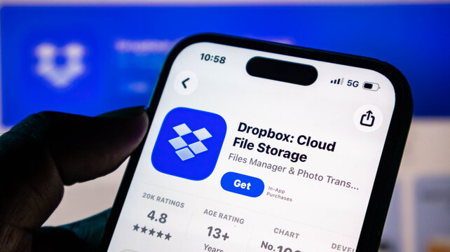 Closeup of a hand holding a smartphone displaying the dropbox app store page on a screen