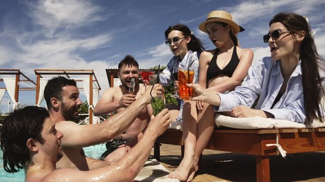 Group of friends having a fun poolside gathering with drinks and relaxed atmosphere. Concept friendship, summer lifestyle and leisure.
