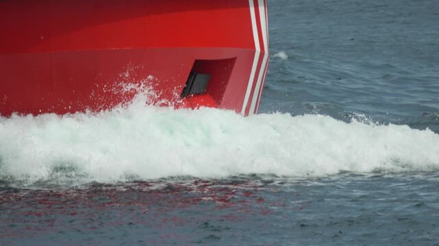 Ship bow wave red vessel cutting through the sea creating white foam and splashes in the ocean water