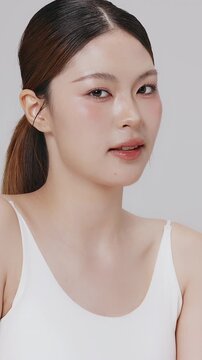 Vertical footage beautiful young Asian woman with healthy facial skin isolated over white background for skincare commercial product advertising. Slow motion shot.