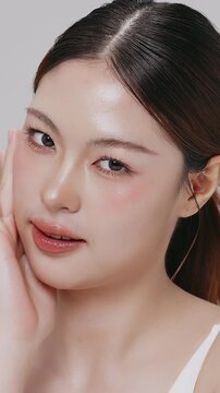 Vertical footage beautiful young Asian woman with healthy facial skin isolated over white background for skincare commercial product advertising. Slow motion shot.