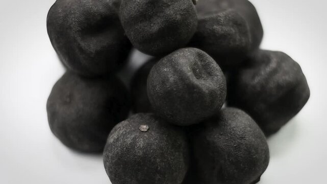 Close-up pile of whole black dried limes - Persian lime loomi textured food ingredient on white