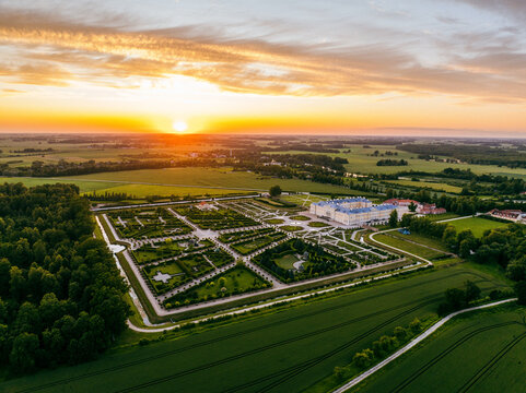 Pilsrundale, Latvia - 04 July 2025: Aerial view of Rundale Palace Museum and its formal French gardens at sunset, surrounded by lush green fields and forests under a golden sky.