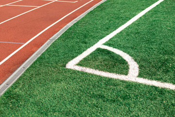 Obraz premium Athletic running track adjacent to a green grass sports field corner