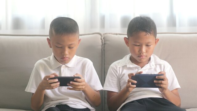 Two Asian children sitting on sofa managing money allowance budget together. Smart boy and girl sorting currency coins near pink piggy bank for future secure financial plan.