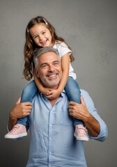 Obraz premium Happy Middle-Aged Father Giving Piggyback Ride to Young Daughter in Studio Portrait on Grey Background