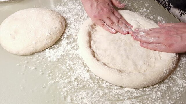 Skilled hands gently stretch and shape a ball of raw pizza dough, creating a perfect base for delicious homemade pizza