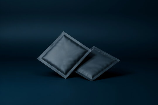 Two blank black matte packaging sachets or condom packets lie flat on a dark blue background showcasing a clean professional product branding presentation mockup template