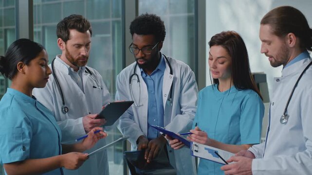 Team five multiethnic doctors talking analyzing patient lung x-ray checkup with digital tablet online medicine service in modern clinic. African American leader doctor talk with coworkers physicians