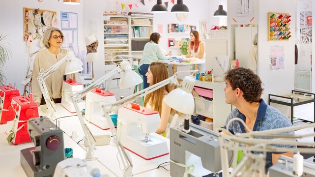 Instructor teaching sewing class to adults in workshop