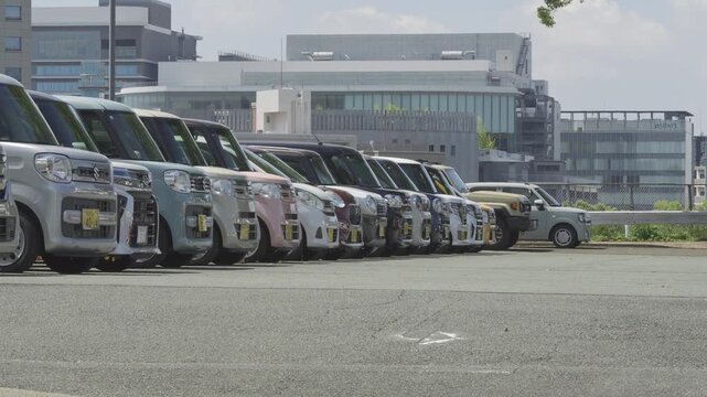 Kei cars or mini vans lined up next to each other in a city public parking area during daytime.