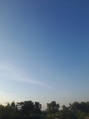 Obraz premium Beautiful and serene view of vast blue sky with white clouds and trees.