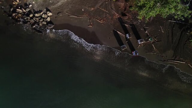 Vertical aerial drone shot rotating clockwise above a tropical shoreline with waves, boats, and
palm trees.