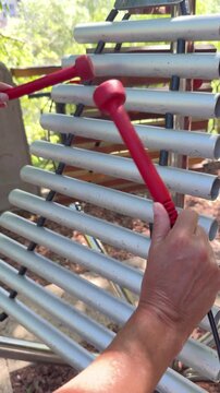 Person demonstrates musical skill while playing a public xylophone in parkland in Oradea, Romania. Vertical 4K footage of an outdoor recreational activity.