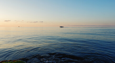 A minimalist wide-angle shot of a calm sea at sunset, featuring a small boat blurred in the distance and natural rock formations in the immediate foreground, perfect for meditation or travel themes © Bilal AKBULUT