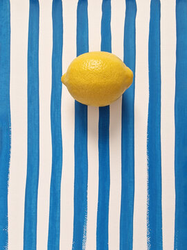  Summer background, food, Mediterranean style concept. Minimalist still life of single whole lemon on hand-painted blue and white striped paper. Top view, space for text.
