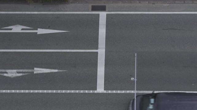 Top down aerial view of a car driving on a city road with white arrow markings.
