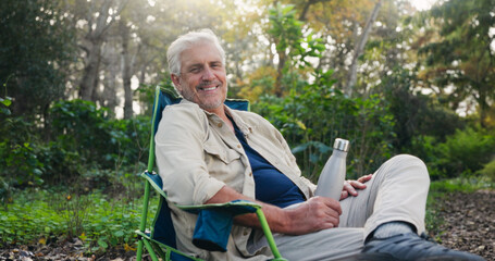 Fototapeta premium Senior, portrait or happy man in nature for camping, outdoor holiday or vacation in wilderness. Elderly, male person or relax with smile, chair or bottle for retirement or weekend getaway on campsite