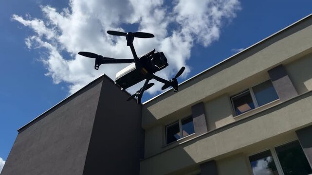 Low angle view of a professional quadcopter drone with rotating propellers flying high in the clear blue sky
